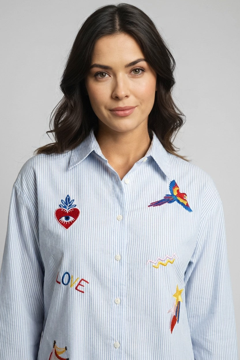 Modelo con camisa de rayas azul y bordados coloridos, vista frontal detalle pecho con loro y corazón bordados