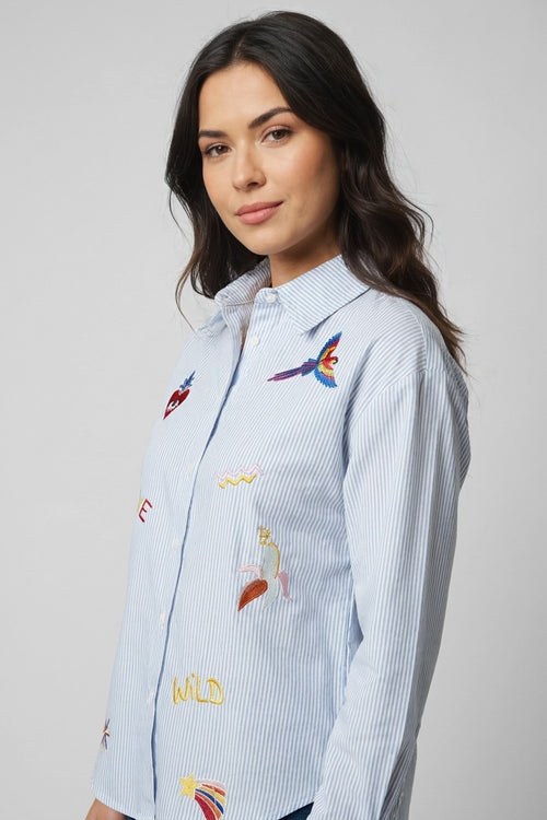 Modelo con camisa de rayas azul Love Wild, vista lateral mostrando bordados WILD y loro en vuelo