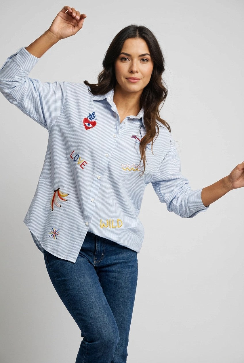 Modelo con camisa de rayas azul holgada y bordados LOVE y WILD, vista completa con vaqueros oscuros en estudio