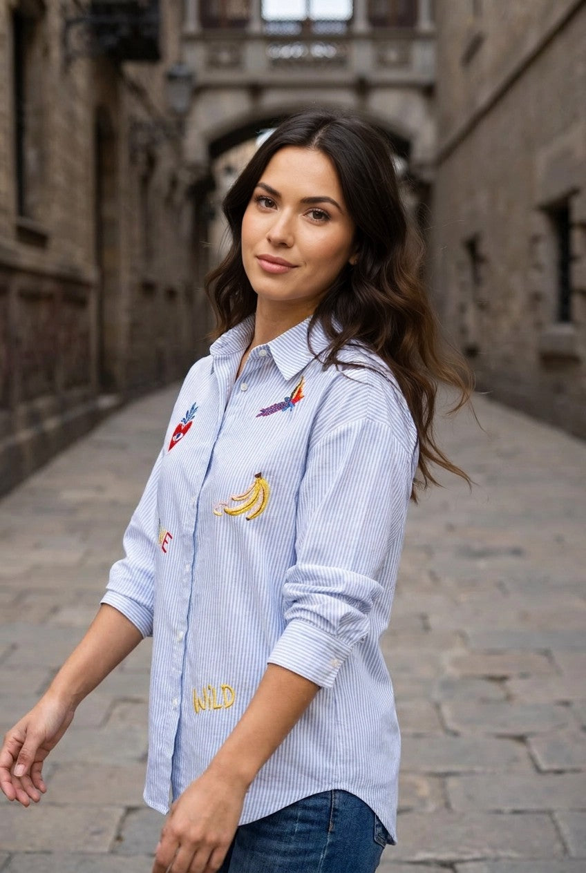 Modelo con camisa de rayas azul bordada en callejón de piedra, vista lateral exterior con mangas recogidas