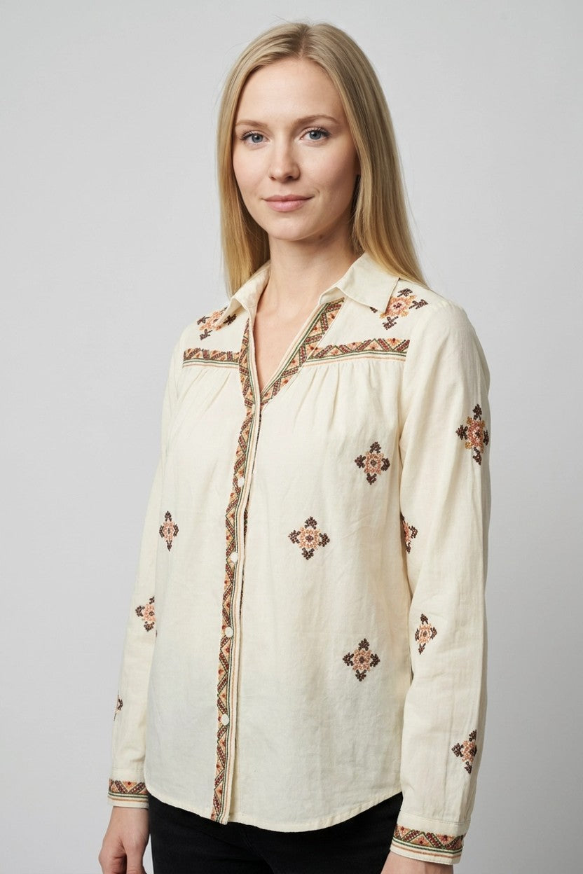 Detalle lateral de blusa beige Mallorca con bordados geométricos en terracota y cuello en pico