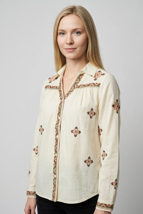 Detalle lateral de blusa beige Mallorca con bordados geométricos en terracota y cuello en pico