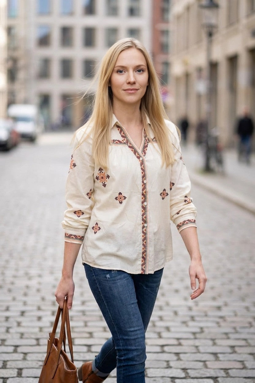 Mujer caminando por calle empedrada con blusa beige Mallorca, vaqueros y bolso camel