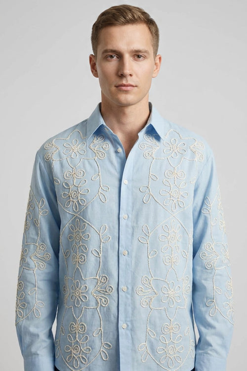 Modelo con camisa azul de manga larga y bordado floral en hilo hueso, vista frontal de estudio
