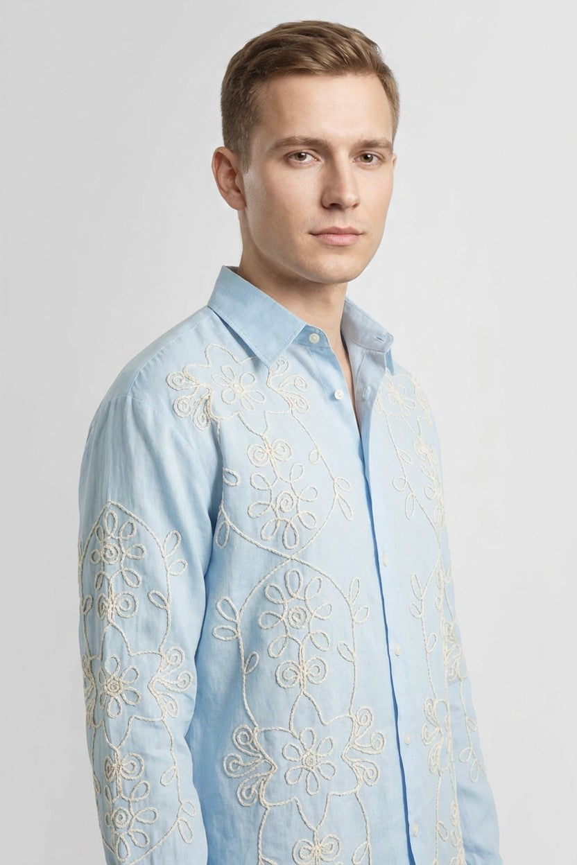 Detalle de camisa azul con bordado floral en hilo hueso, vista de tres cuartos