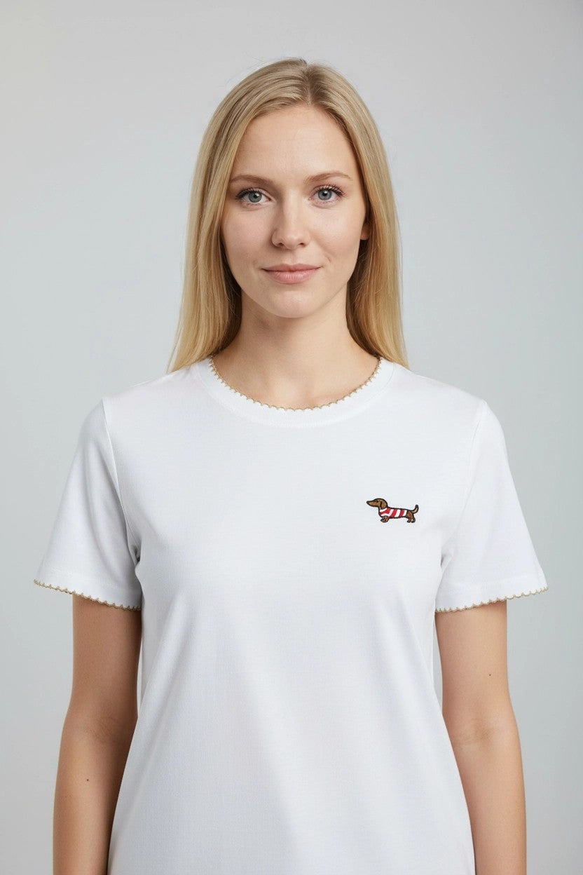 Camiseta blanca con ribete dorado y teckel bordado en pecho, vista frontal de estudio