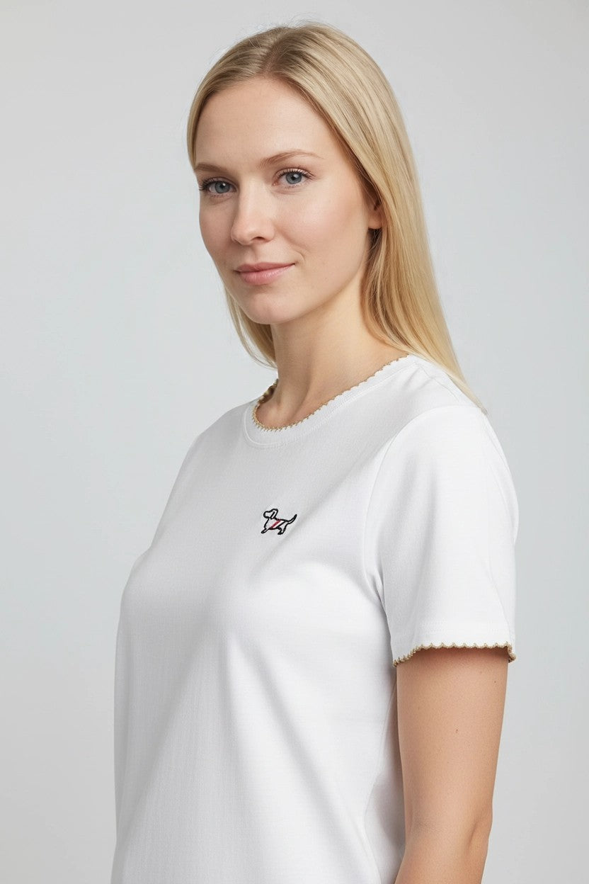 Detalle lateral de camiseta blanca con ribete dorado en cuello y puños y teckel bordado