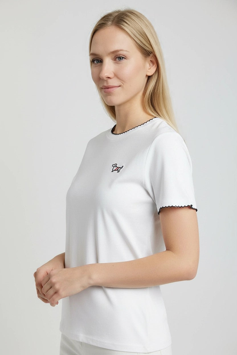 Detalle lateral de camiseta blanca con ribete negro en cuello y puños y teckel bordado