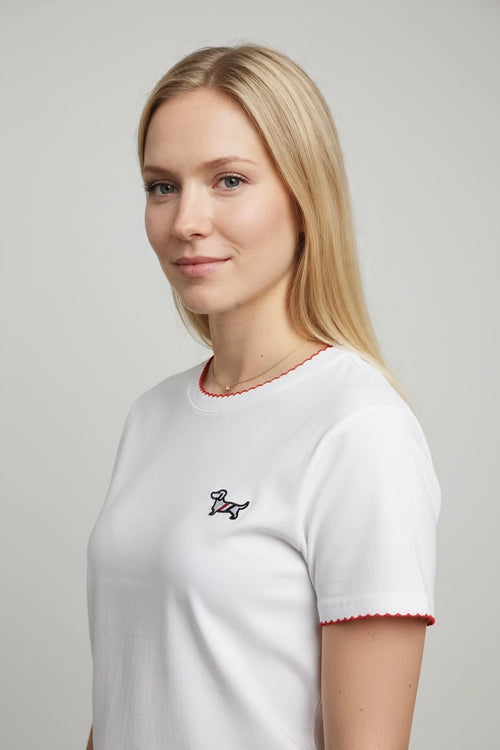 Detalle lateral de camiseta blanca con ribete rojo en cuello y puños y teckel bordado
