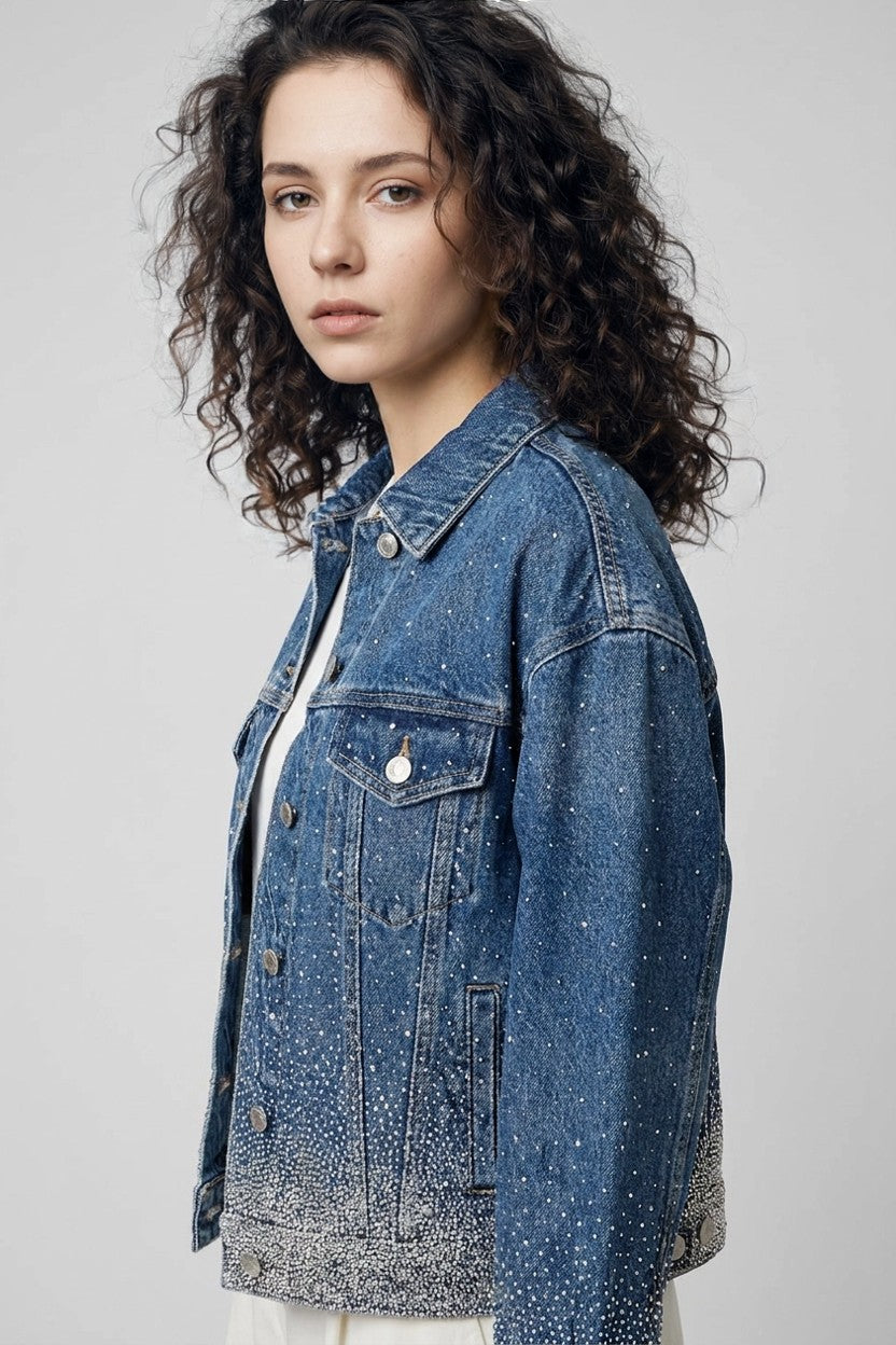 Detalle lateral de chaqueta denim azul con strass concentrados en bajo y puños, vista de perfil