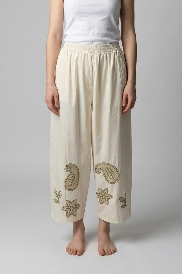 Mujer con pantalón baggy beige y bordados paisley en los bajos, vista frontal de estudio