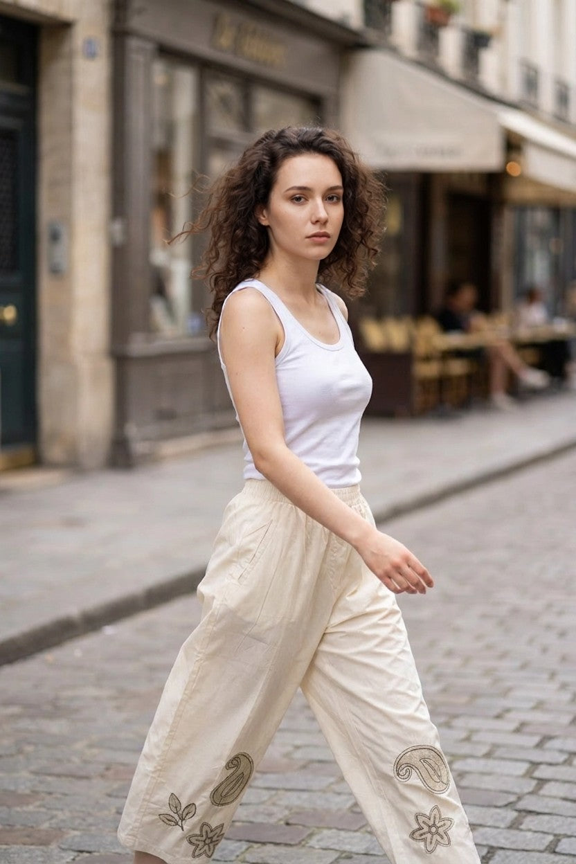 Modelo paseando por calle empedrada con pantalón baggy beige bordado y camiseta blanca