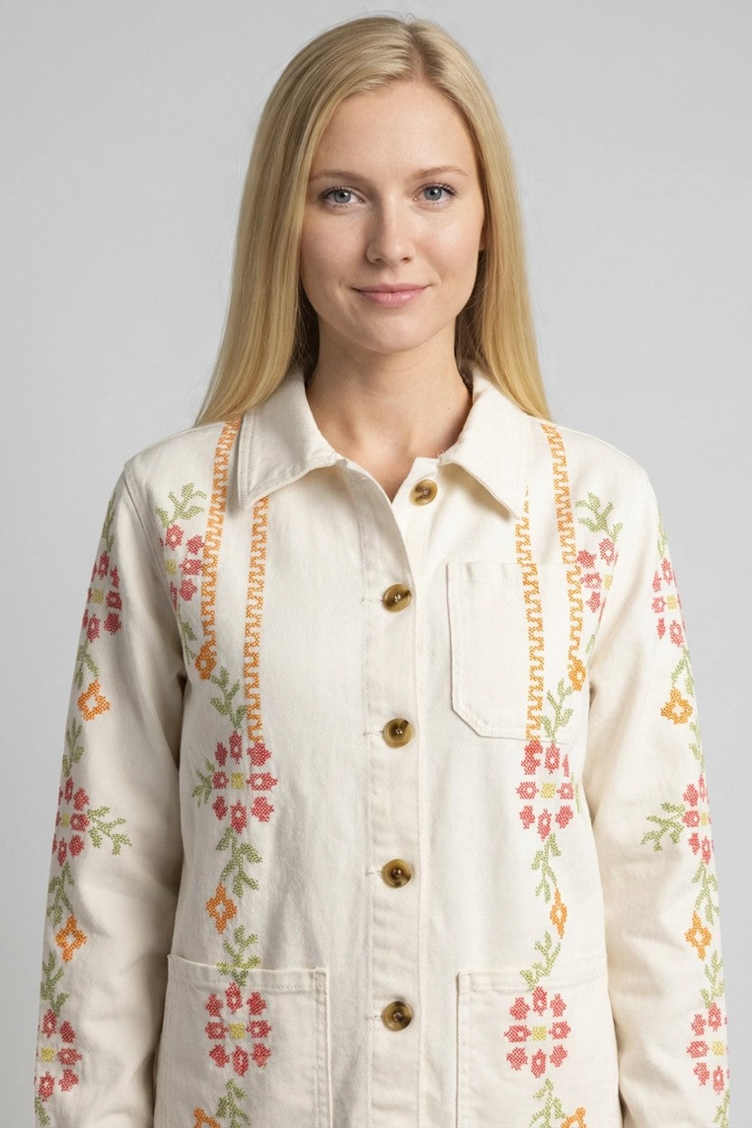 Mujer con chaqueta blanca y bordado floral en punto de cruz, detalle del delantero en estudio