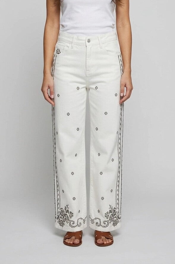 Mujer con pantalón vaquero ancho blanco y bordado de punto de cruz, vista frontal de estudio