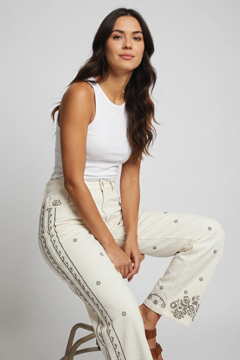 Modelo sentada con pantalón vaquero wide leg blanco bordado y top blanco, plano tres cuartos