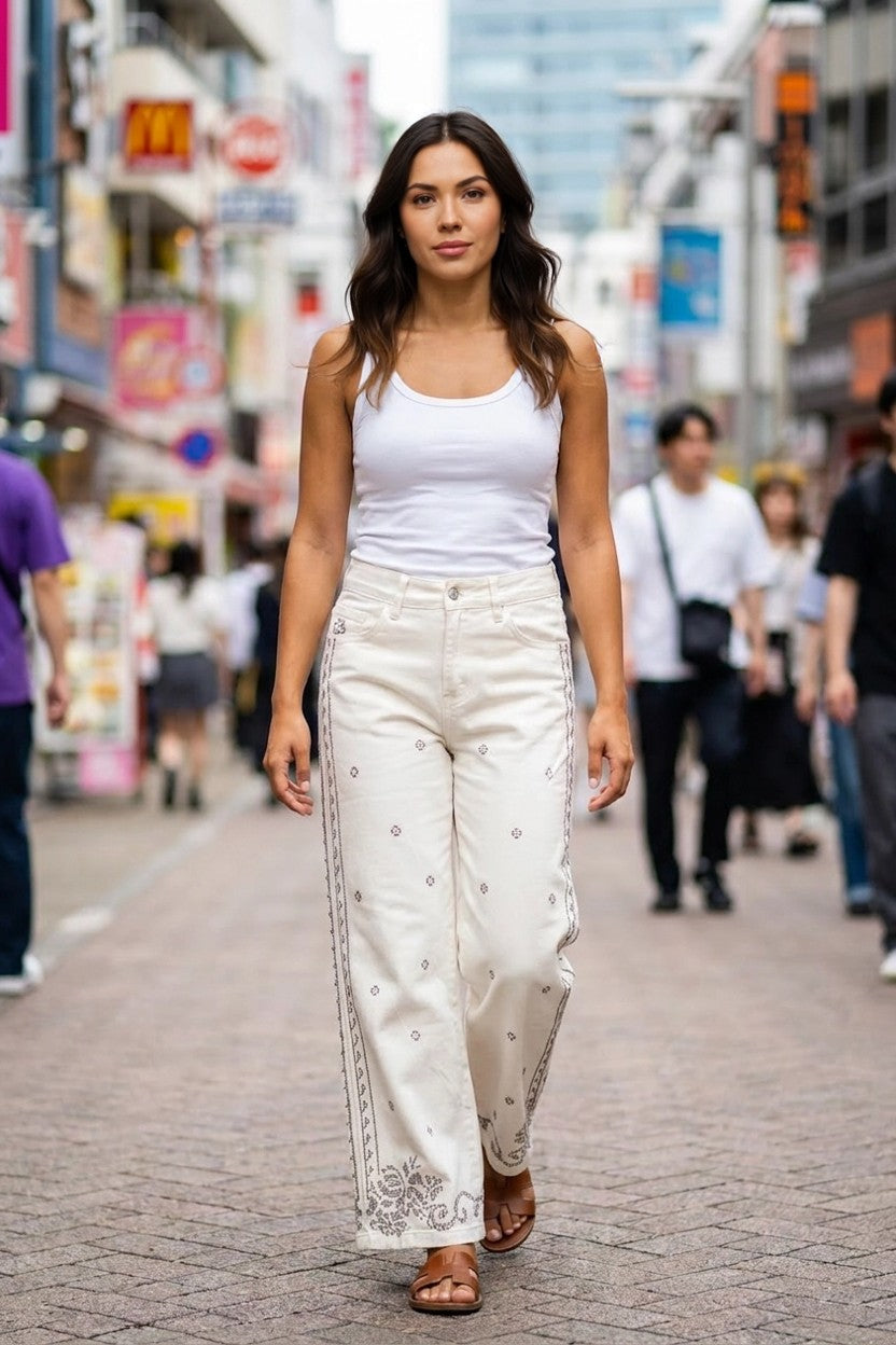 Mujer caminando por calle con pantalón vaquero blanco de punto de cruz y top blanco, look street style
