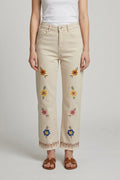 Mujer con pantalón beige de flores bordadas, vista frontal de estudio, combinado con camiseta blanca y sandalias