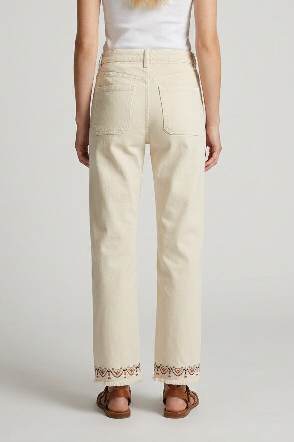 Vista trasera del pantalón beige con cenefa bordada y bajo deshilachado, detalle de bolsillos traseros