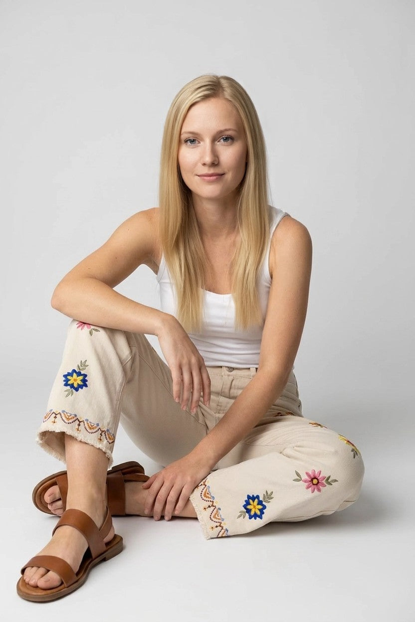 Modelo sentada en estudio con pantalón beige floral, detalle de bordados y cenefa en el bajo