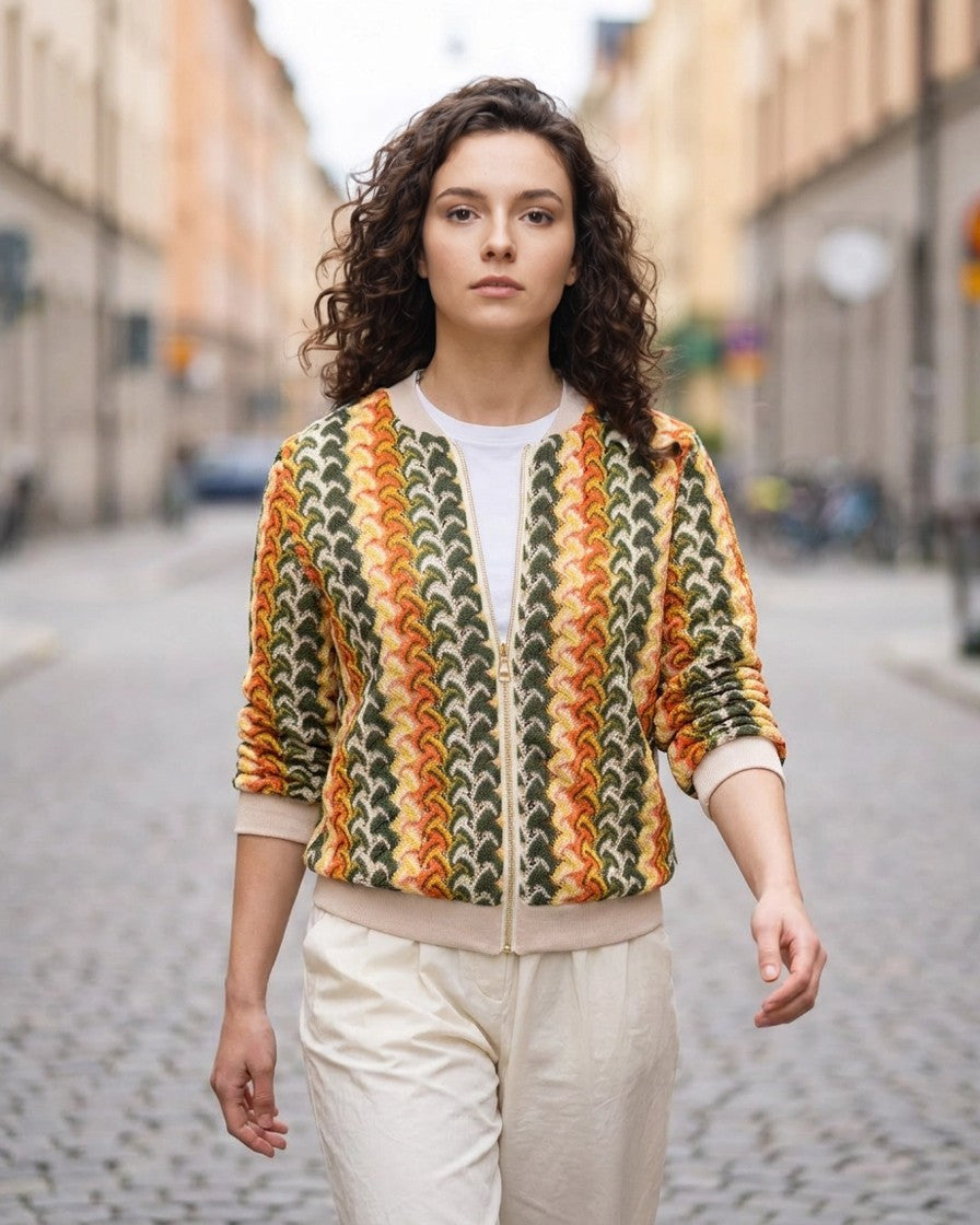Mujer con chaqueta bomber de punto jacquard tricolor en exteriores, look calle con pantalón blanco