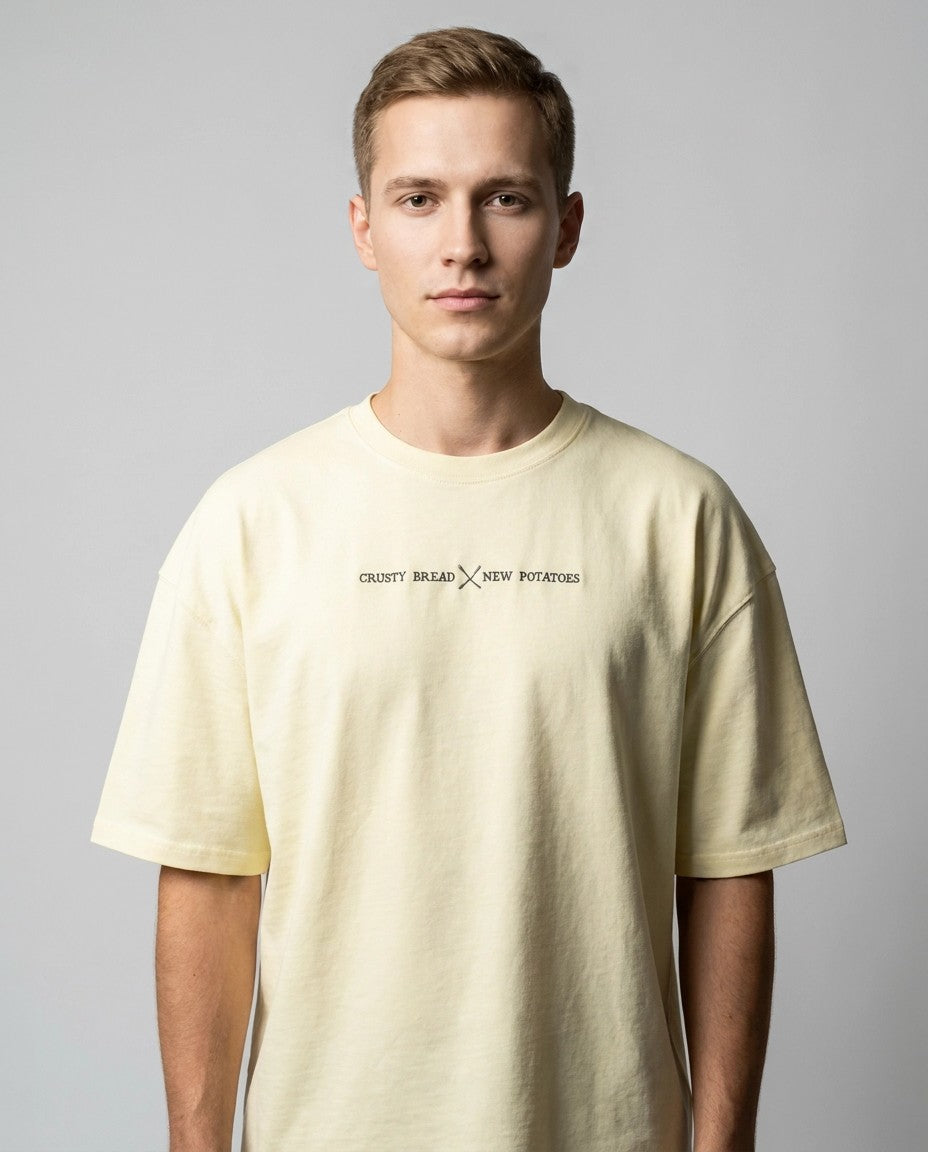 Hombre con camiseta oversize cruda y texto bordado Crusty Bread x New Potatoes, vista frontal de estudio