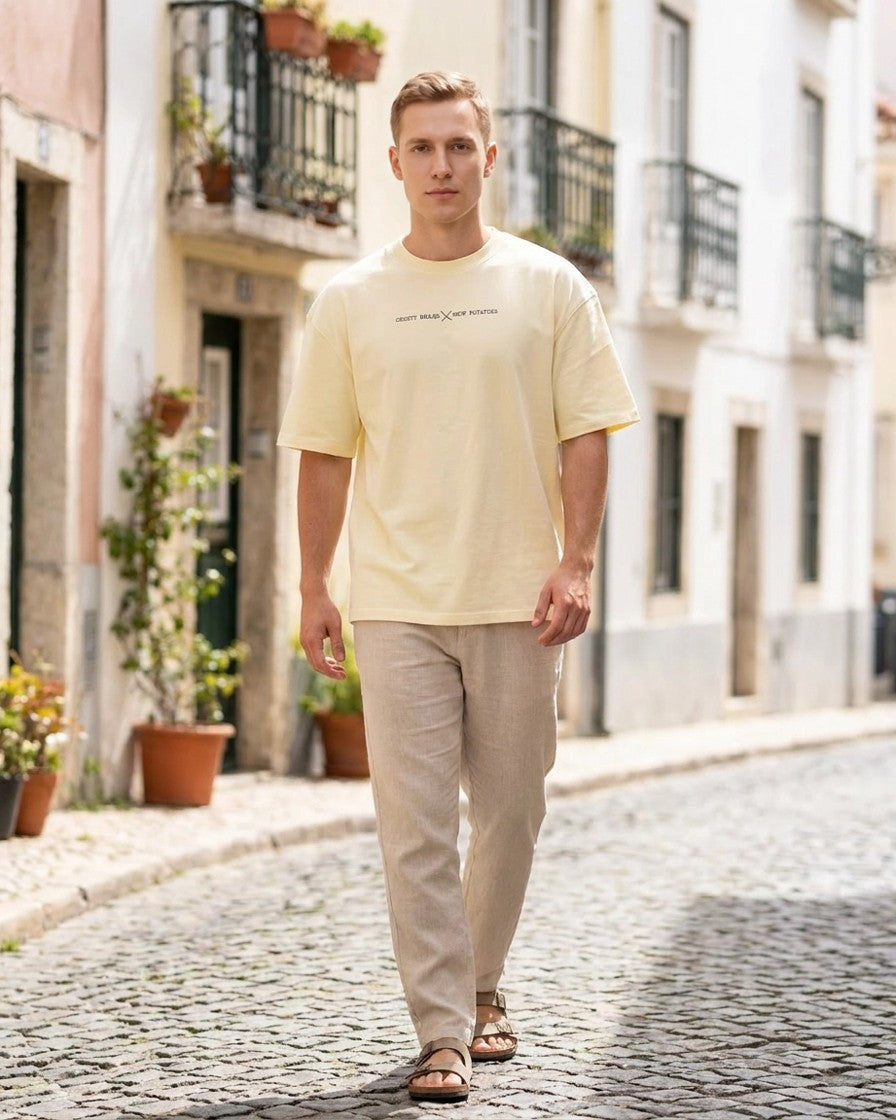 Hombre con camiseta oversize cruda caminando por calle empedrada, look completo con pantalón beis