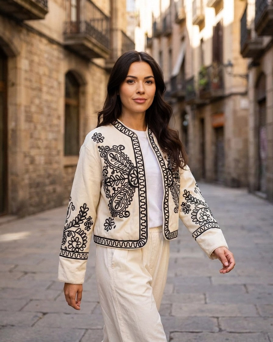 Modelo con chaqueta torera beige bordada caminando por calle empedrada